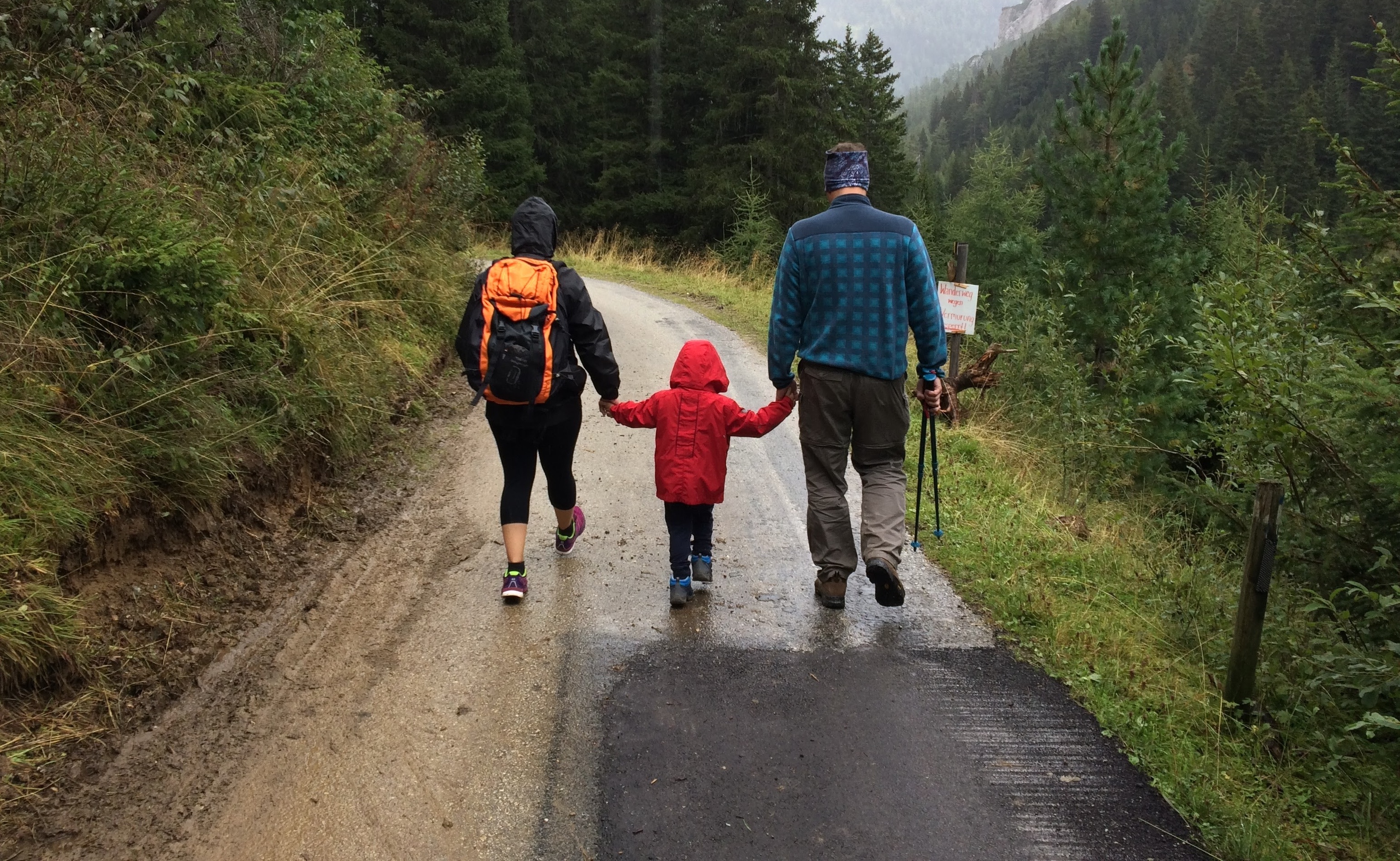 A mother and father walking down a trail outside with their child