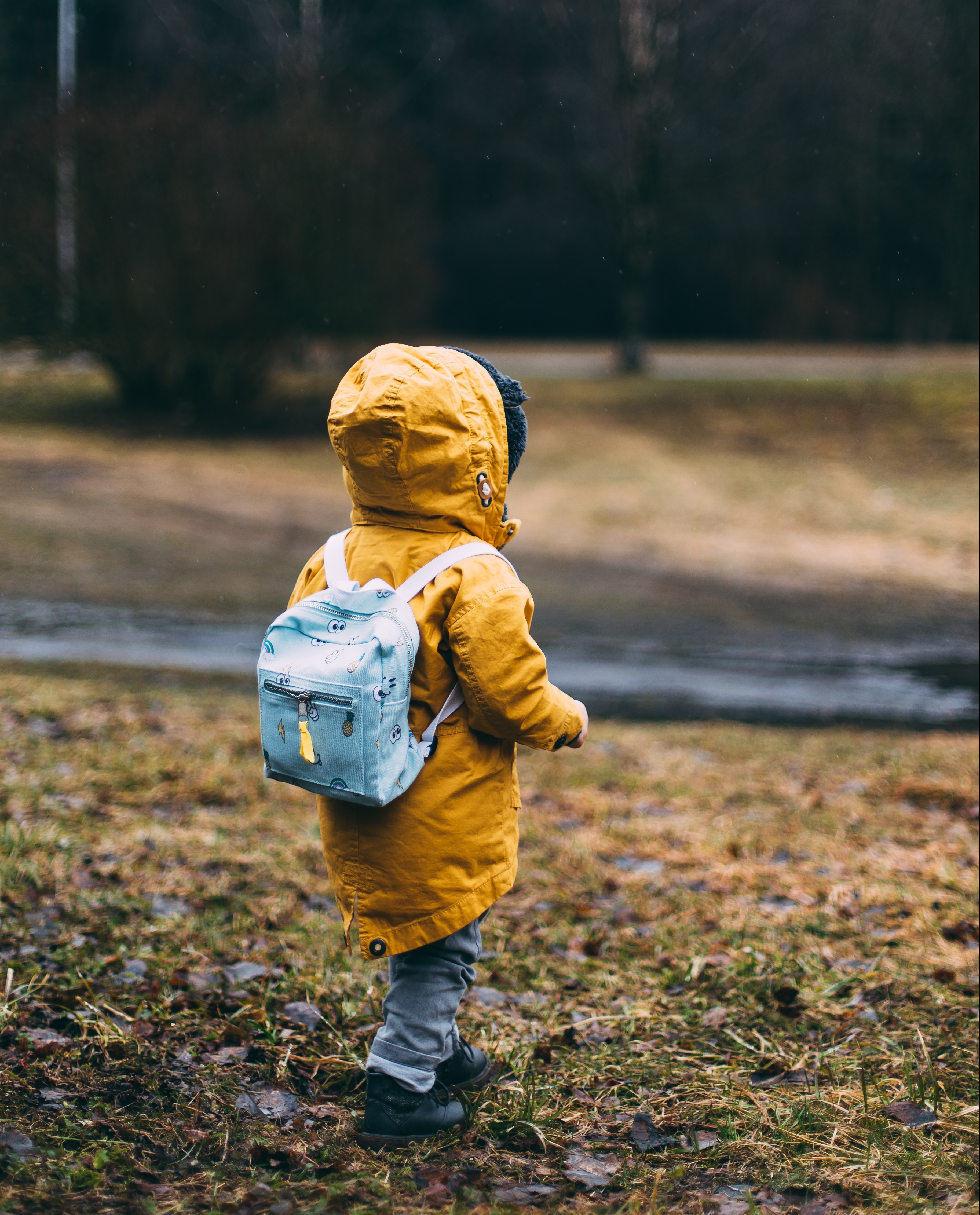 Child in yellow jacket with a blue backpack outside